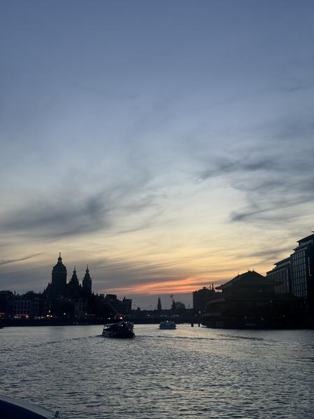 A beautiful sunset paints the sky with warm hues over the water, silhouetting the city skyline of Amsterdam